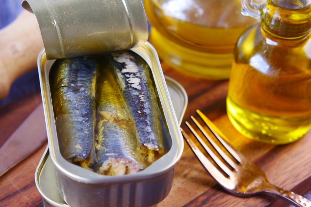 A container of sardines is positioned on a table, accompanied by a fork resting beside it.